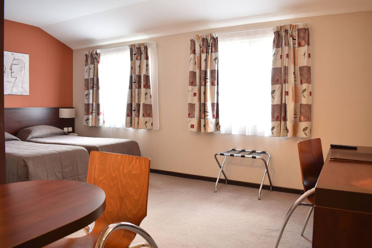 A hotel room with two beds, a desk, a chair, and a small table.