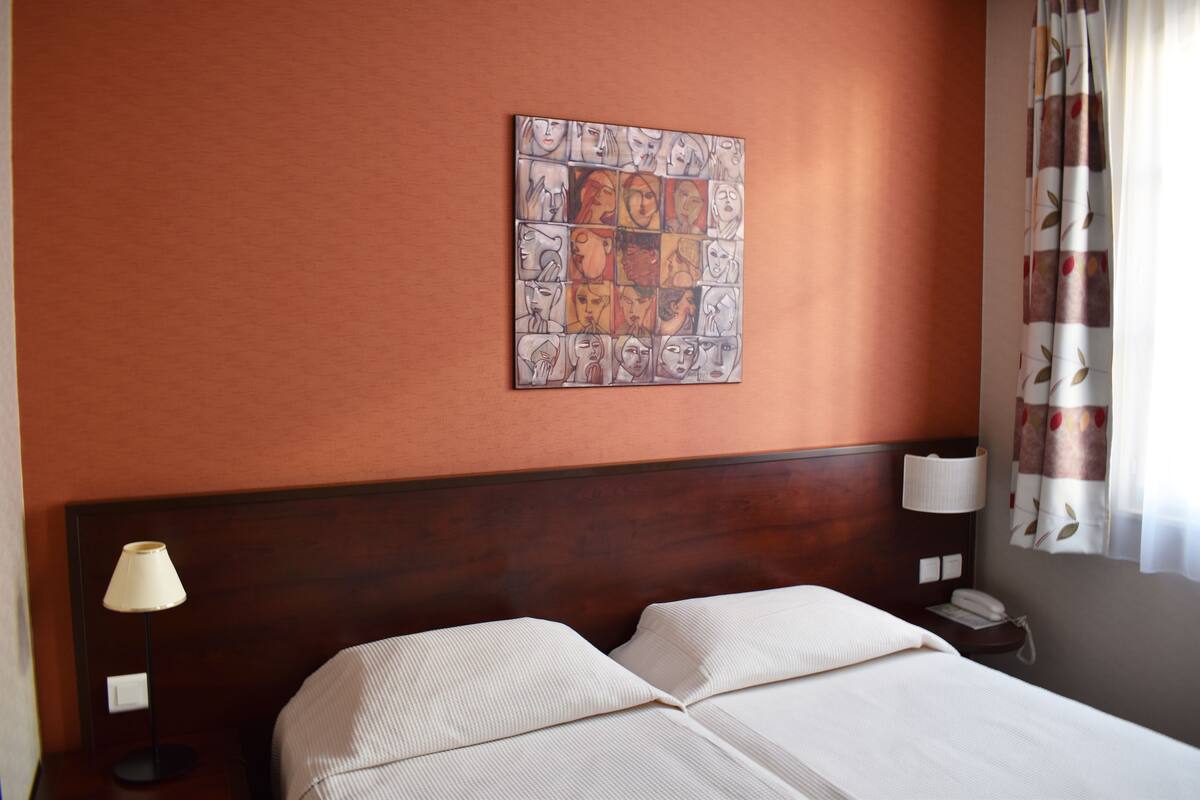 A hotel room with a large bed, a headboard, a wall-mounted artwork, a nightstand with a lamp, and a telephone.