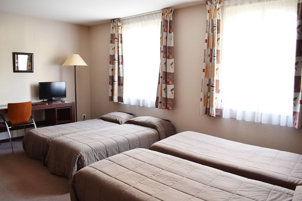 A hotel room with two single beds, a desk with a chair, a television, and curtains on the windows.