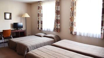Une chambre d’hôtel avec deux lits simples, un bureau avec une chaise, une télévision et des rideaux aux fenêtres.