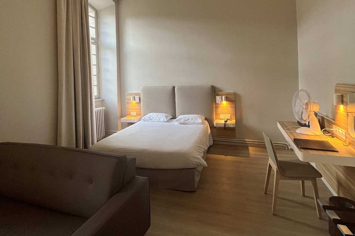 A hotel room with a bed, a desk, a chair, and a sofa.