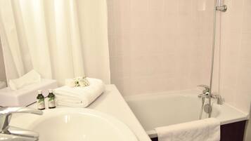 A bathroom with a bathtub, a sink, and a shower. There are towels and toiletries on the counter.