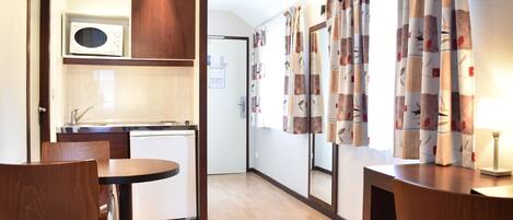 A compact kitchen with a microwave, a small refrigerator, and a wooden cabinet. There is a dining area with a table and chairs.