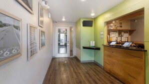A hallway with framed pictures on the wall, a reception desk with computers, and a door leading to another room. - Extended Stay America Select Suites - Phoenix - West (Phoenix)