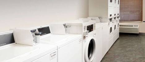 A laundry facility with multiple washing machines and dryers, a ventilation system, and a window with blinds.