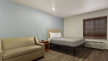 A bedroom with a bed, a sofa, a nightstand, and a window with blinds.