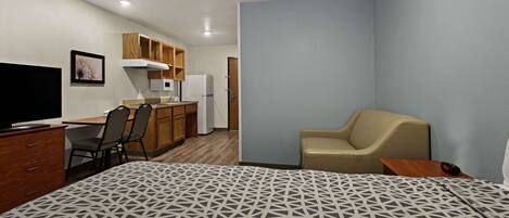 Una habitación de hotel compacta con cama, escritorio con silla, kitchenette y televisor.