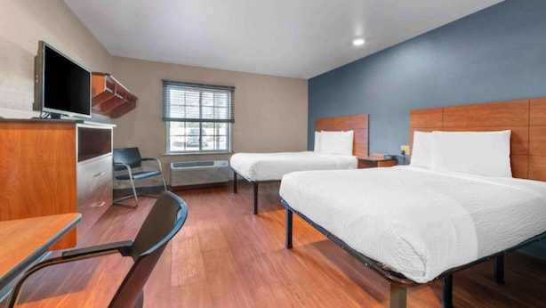 A hotel room with two beds, a desk, a chair, a television, and a window with blinds. - Studio 6 Extended Stay Birmingham Pelham  AL (Pelham)