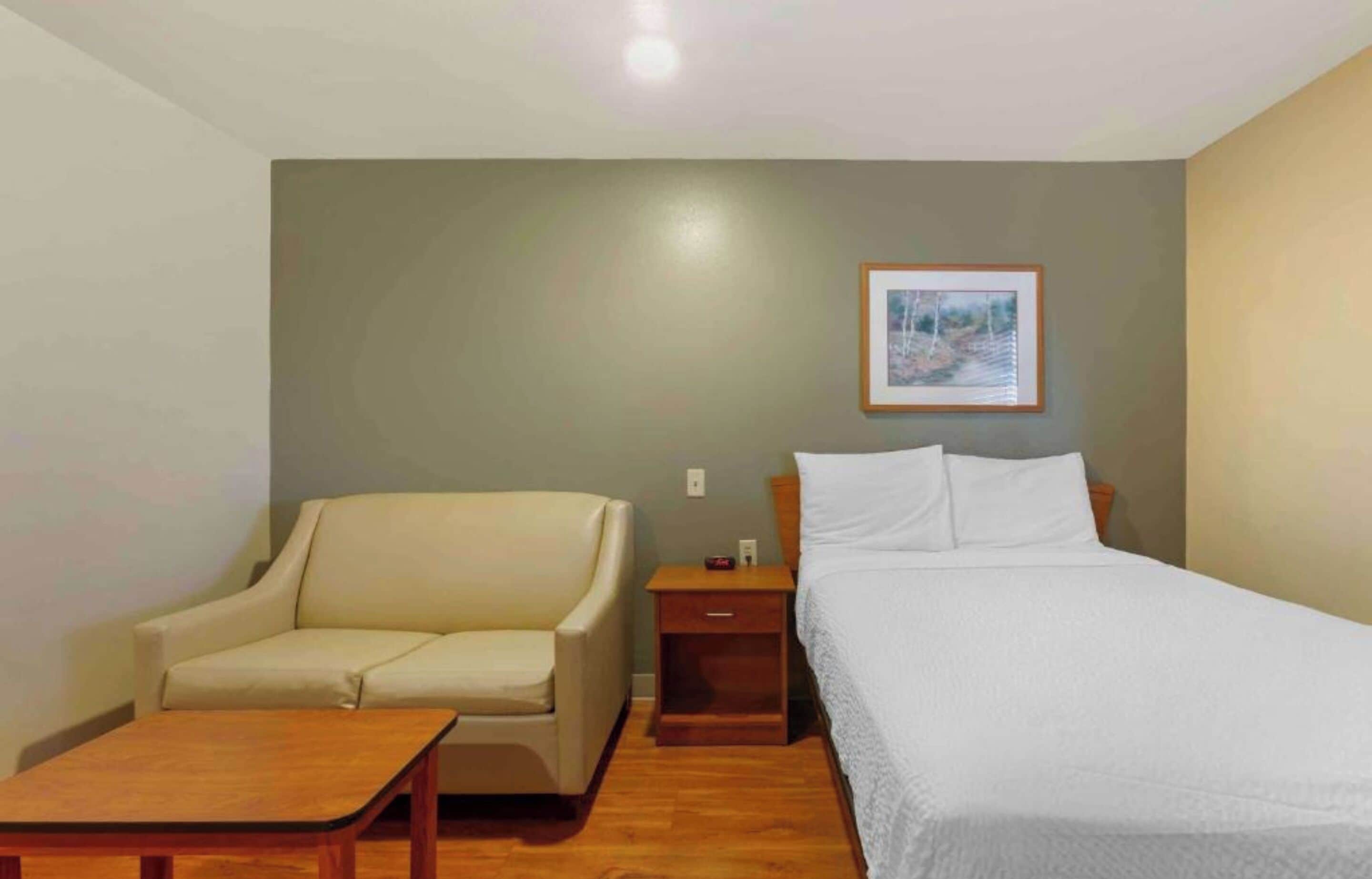 Una habitación con cama, una silla, una mesita y una mesita de noche.