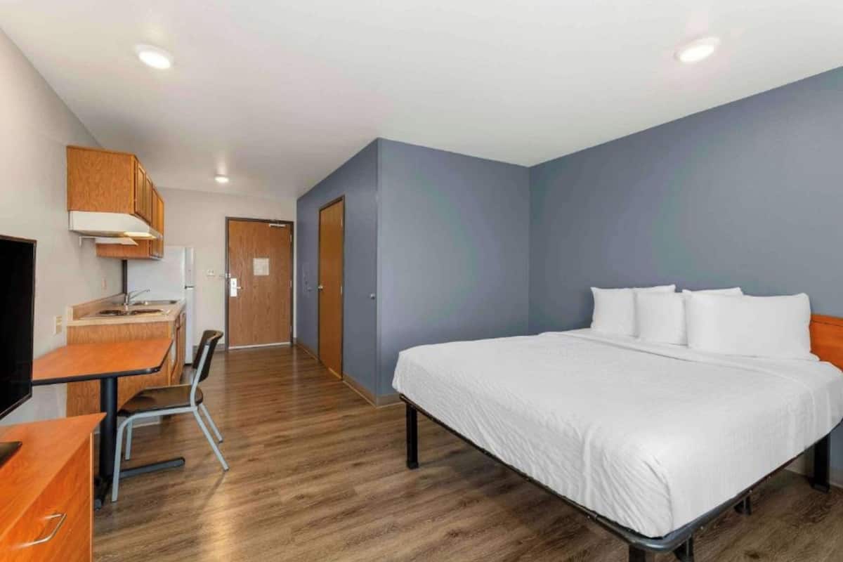 A hotel room with a bed, a desk with a chair, a television, and a door.