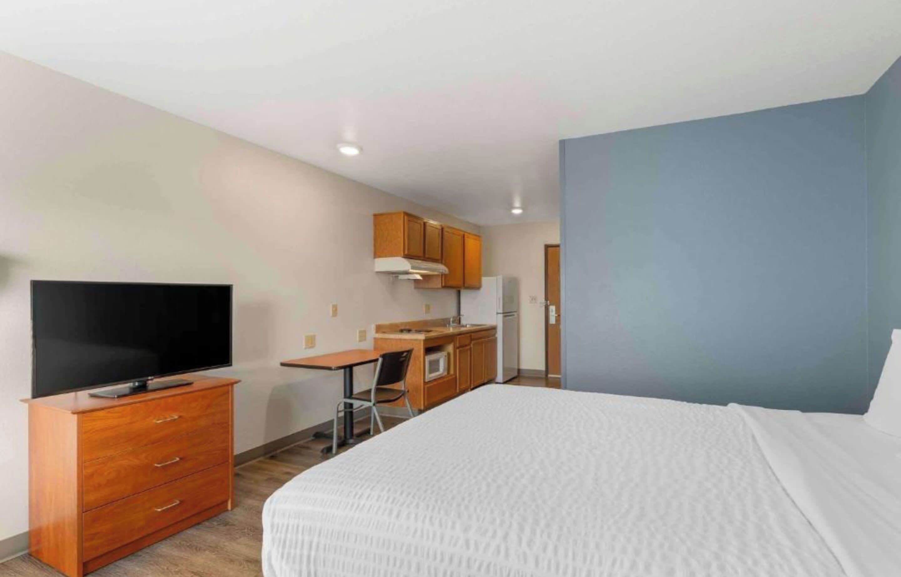 A hotel room with a bed, a TV, a desk, and a kitchenette.