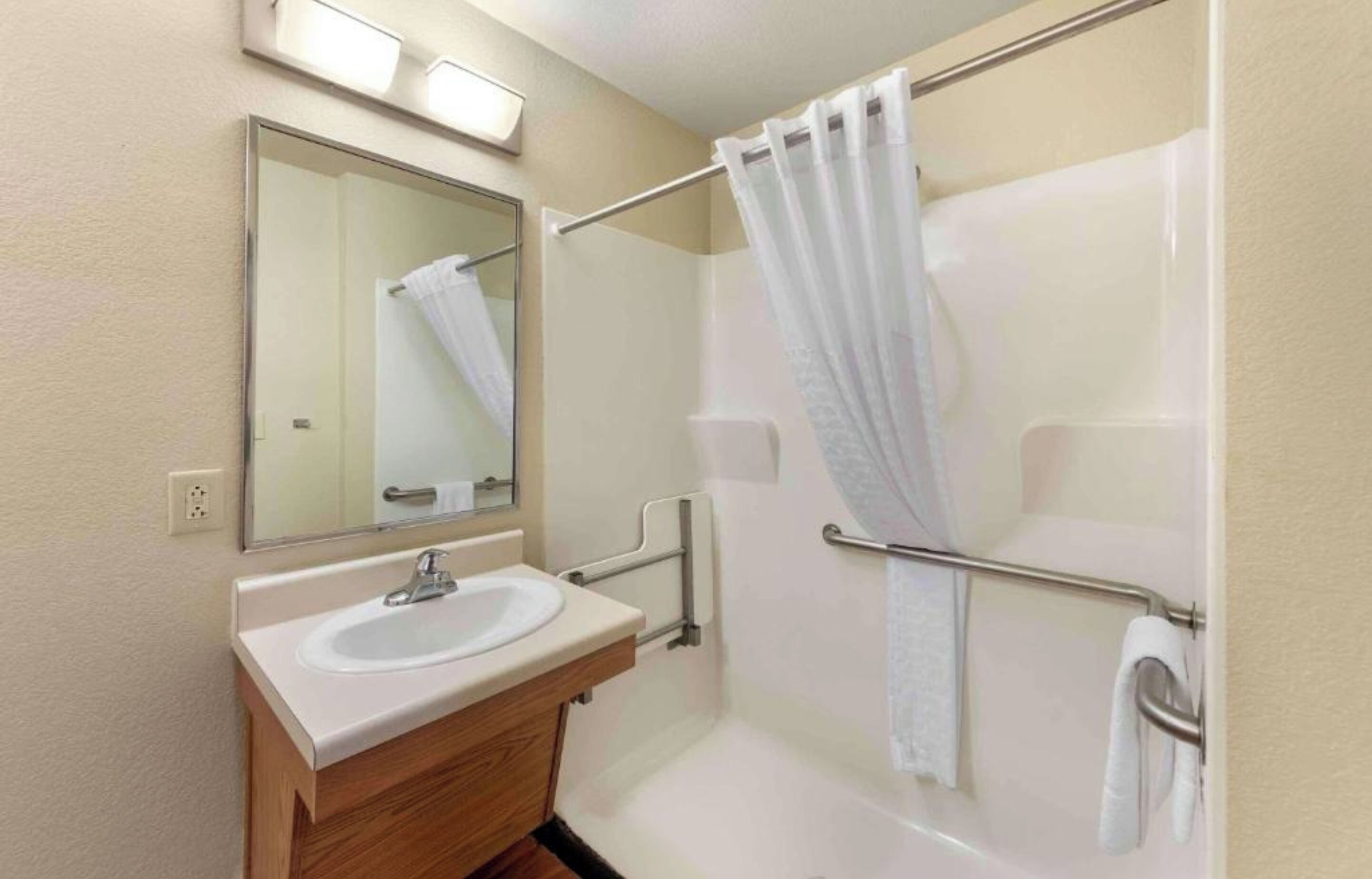 A bathroom with a sink, mirror, shower, and grab bars.