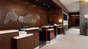 A hotel reception area with wooden paneling, a large decorative wall piece, and a reception desk labeled "MARRIOTT BONNEVILLE". - The Westin Reston Heights (Reston)