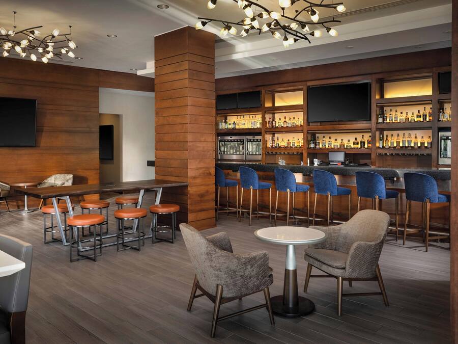 Angolo bar con rivestimenti in legno, bancone, sedie blu e diverse bottiglie.