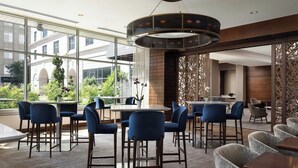 A modern indoor seating area with bar stools and tables, large windows offering a view of the outdoors, and a decorative ceiling light fixture. - The Westin Reston Heights (Reston)