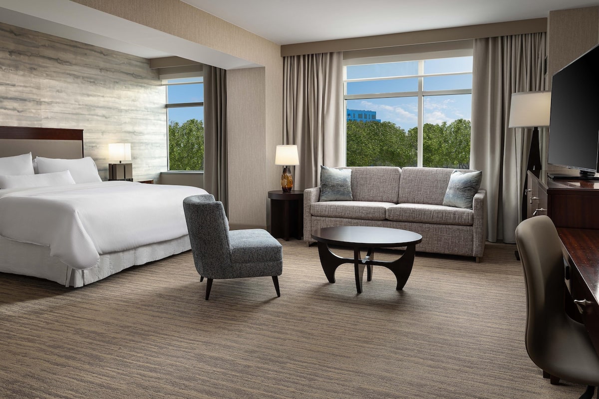A hotel room with a large bed, a sofa, a chair, a coffee table, and a TV.