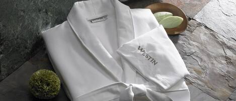 A neatly folded white garment with a Westin logo, a small green decorative item, and a wooden bowl with a white object on a stone floor.