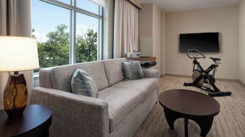 Een hotelkamer met een bank, een bijzettafeltje, een aan de muur bevestigde televisie en een hometrainer.
