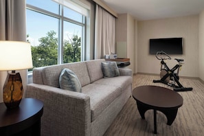 A hotel room with a sofa, a small table, a TV mounted on the wall, and an exercise bike.