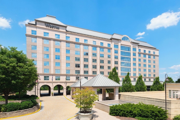 A large, multi-story hotel with a prominent "Westin" sign, featuring a central entrance with a covered walkway and a small garden area.