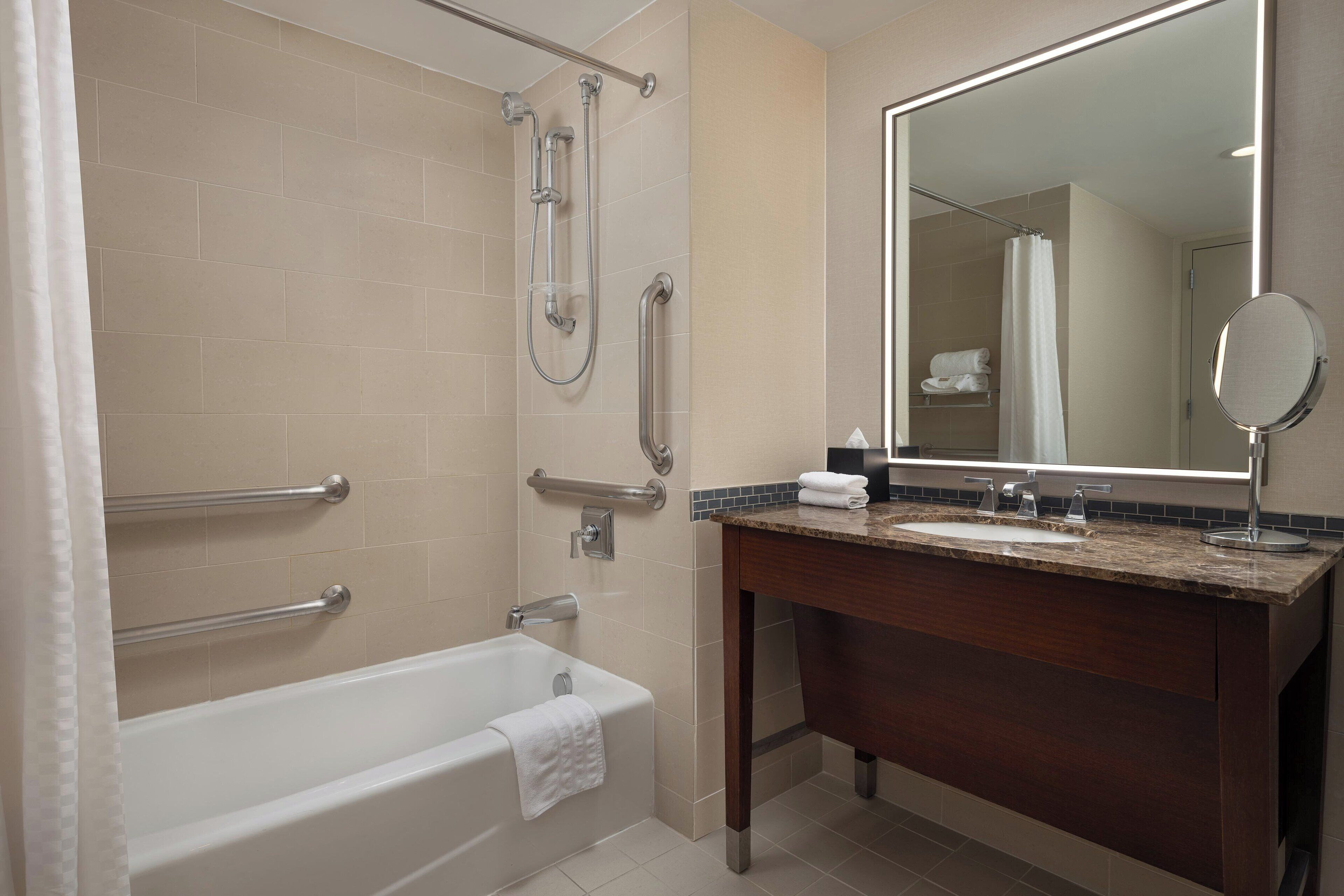 A modern bathroom with a bathtub, shower, vanity, and a large mirror.