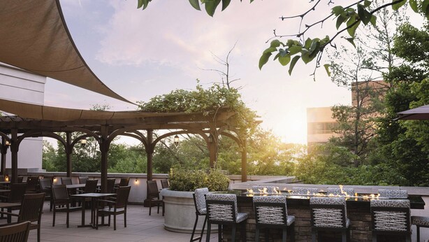 An outdoor patio area with tables and chairs, a stone bar, and a pergola with string lights. - The Westin Reston Heights (Reston)