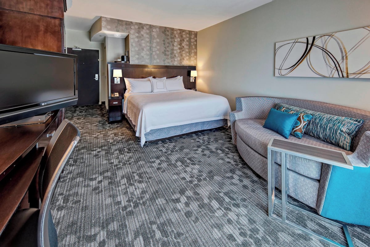 A hotel room with a large bed, a TV, a sofa, and a small table.