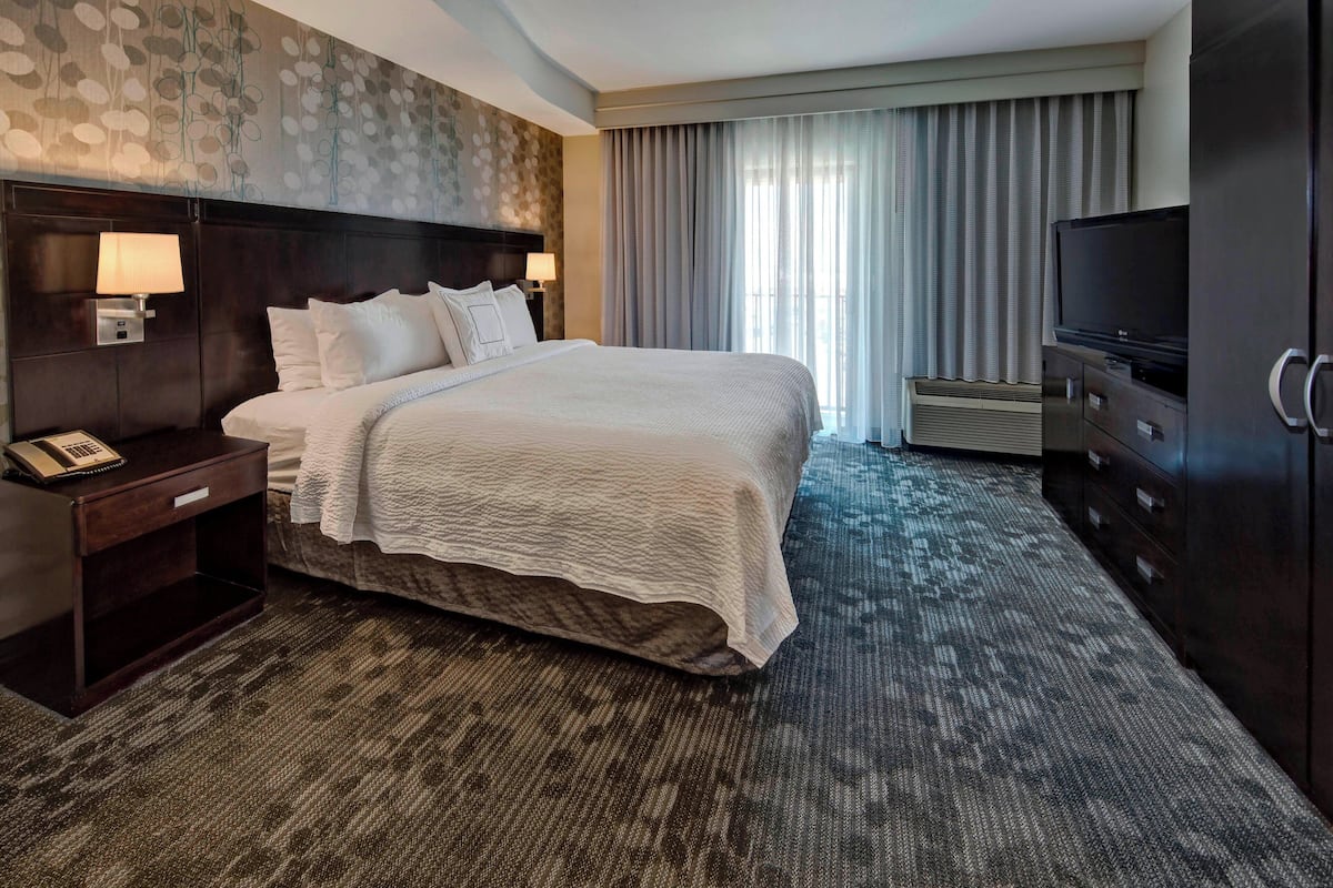 A hotel room with a large bed, a TV, a desk with a lamp, and a telephone.