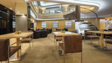 A modern hotel lobby with a central staircase, multiple seating areas, and a high ceiling with integrated lighting.
