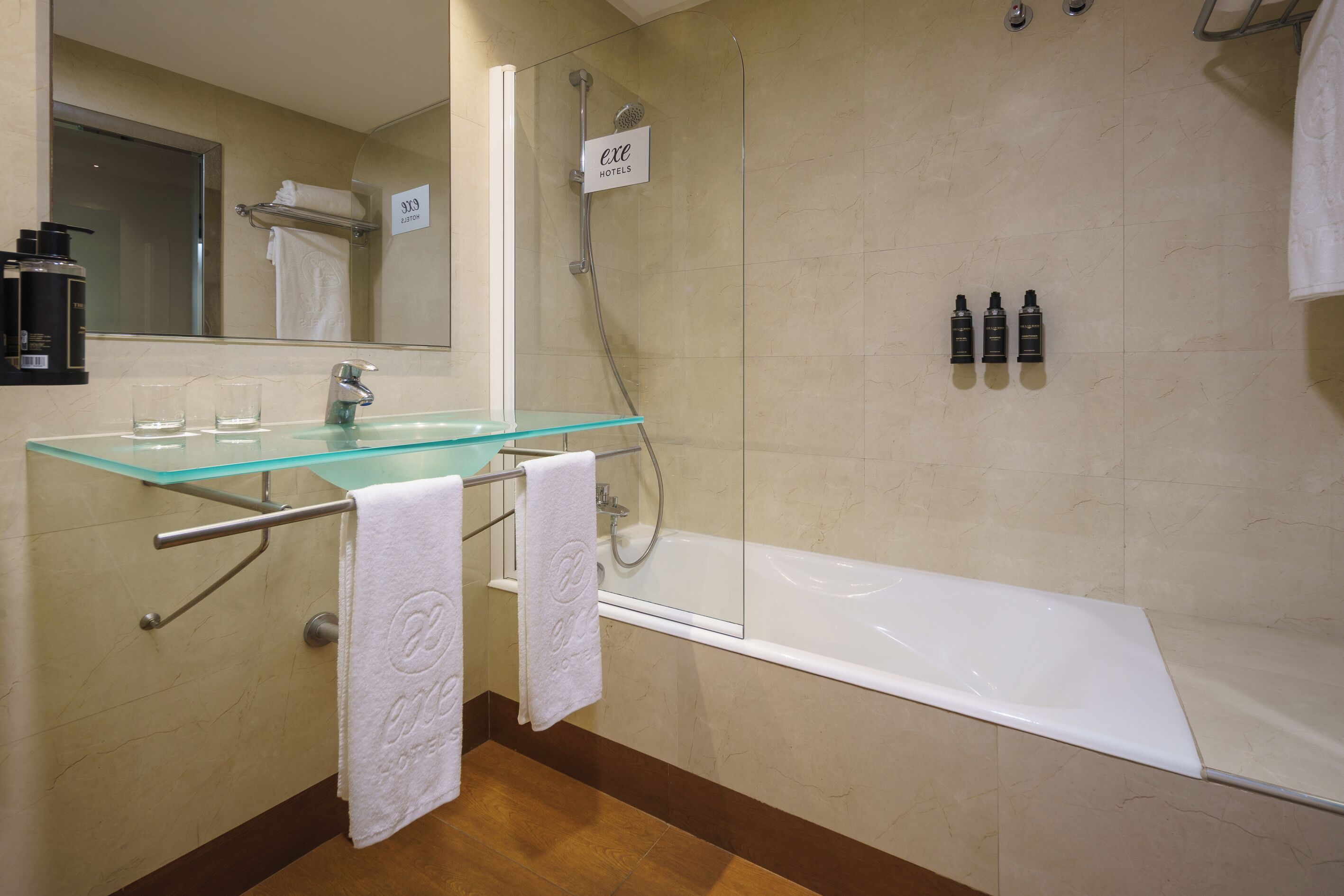 A modern bathroom with a glass-topped sink, a white bathtub, and a glass-enclosed shower.
