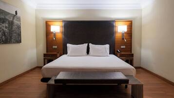 Habitación de hotel con una cama grande, dos mesitas de noche, un banco al pie de la cama y una obra de arte colgada en la pared.