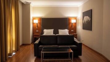 Habitación de hotel con sofá de cuero oscuro, una mesita pequeña, dos lámparas de noche y un cuadro enmarcado en la pared.