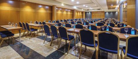 A conference room with rows of tables and chairs, equipped with water bottles and glasses.