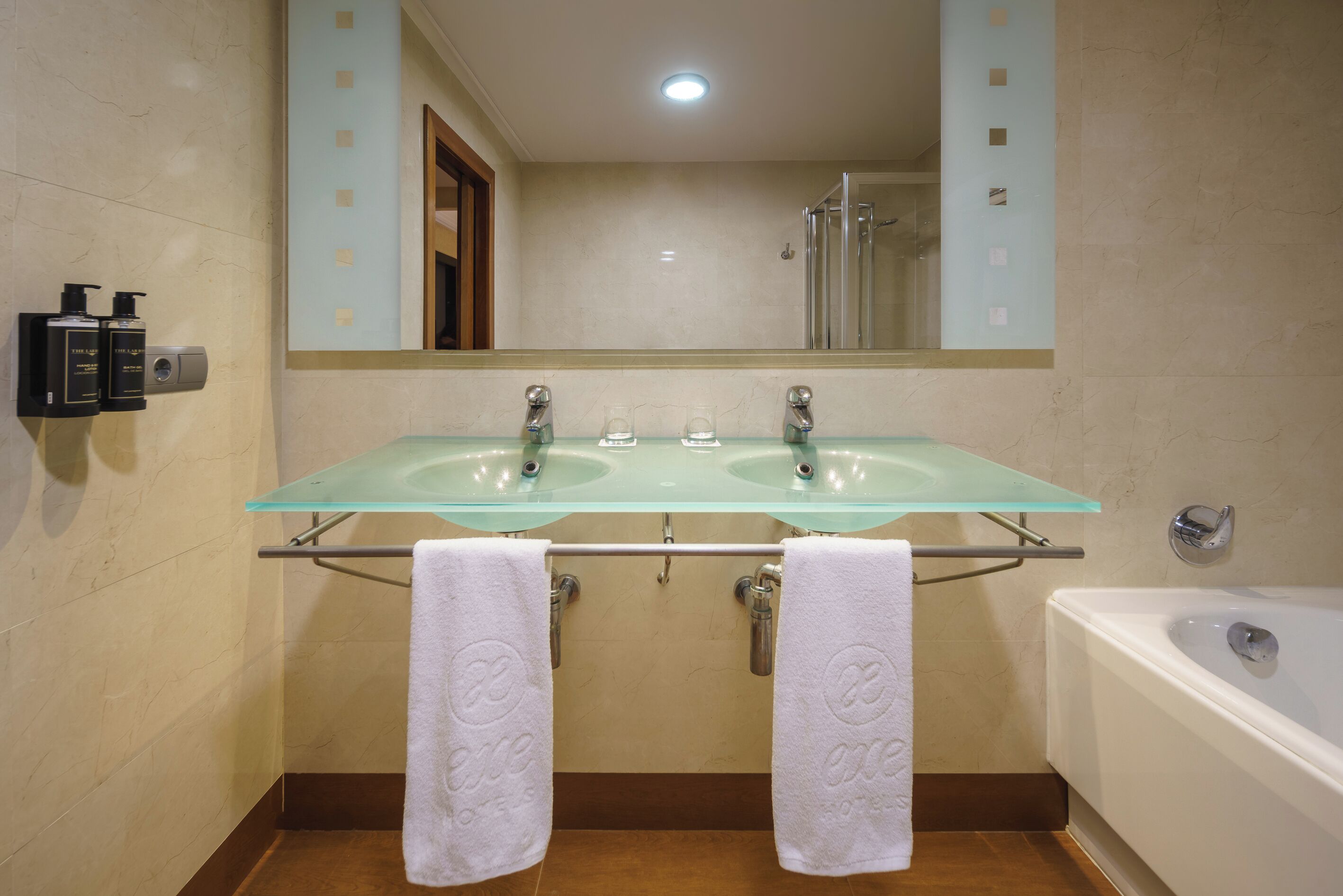 A bathroom with two glass sinks, a large mirror, a bathtub, and two towels hanging on a rack.