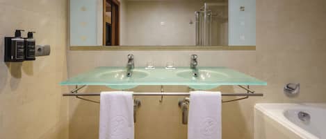 A bathroom with two glass sinks, a large mirror, a bathtub, and two towels hanging on a rack.