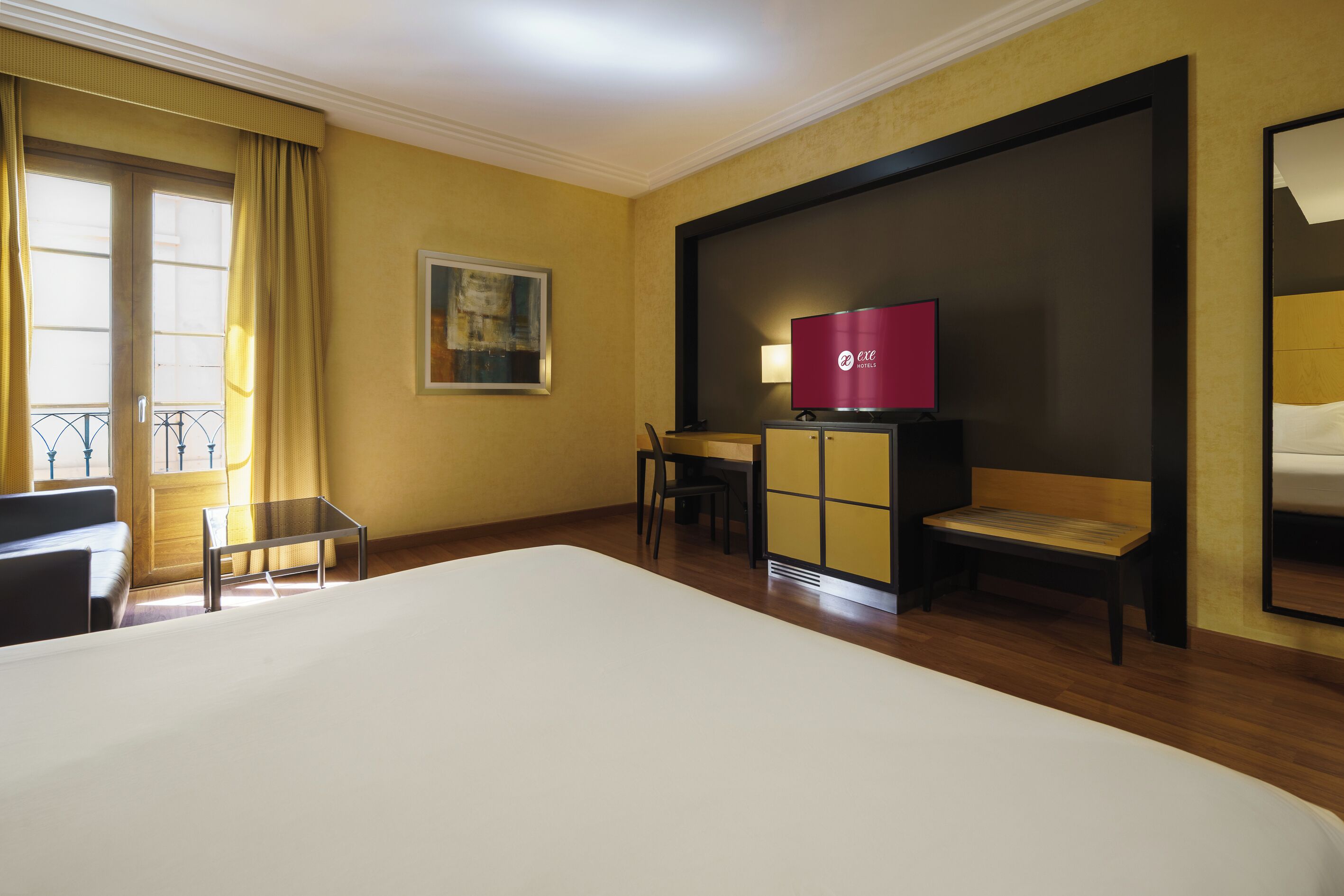 Una habitación de hotel con una cama grande, un escritorio con silla, un televisor y un cuadro en la pared.