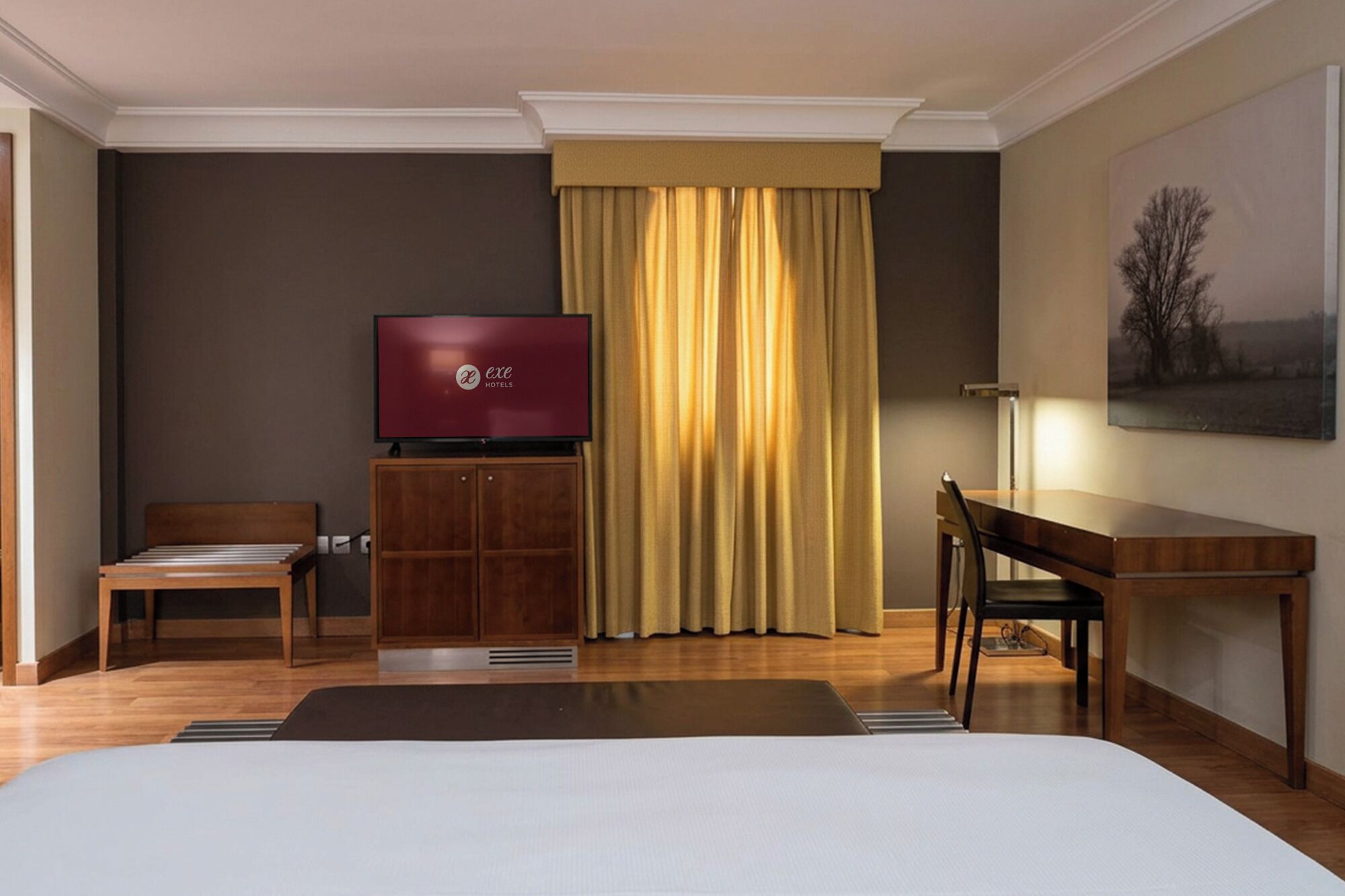 Ein Hotelzimmer mit Bett, Schreibtisch, Stuhl, Fernseher und einem Bild an der Wand.