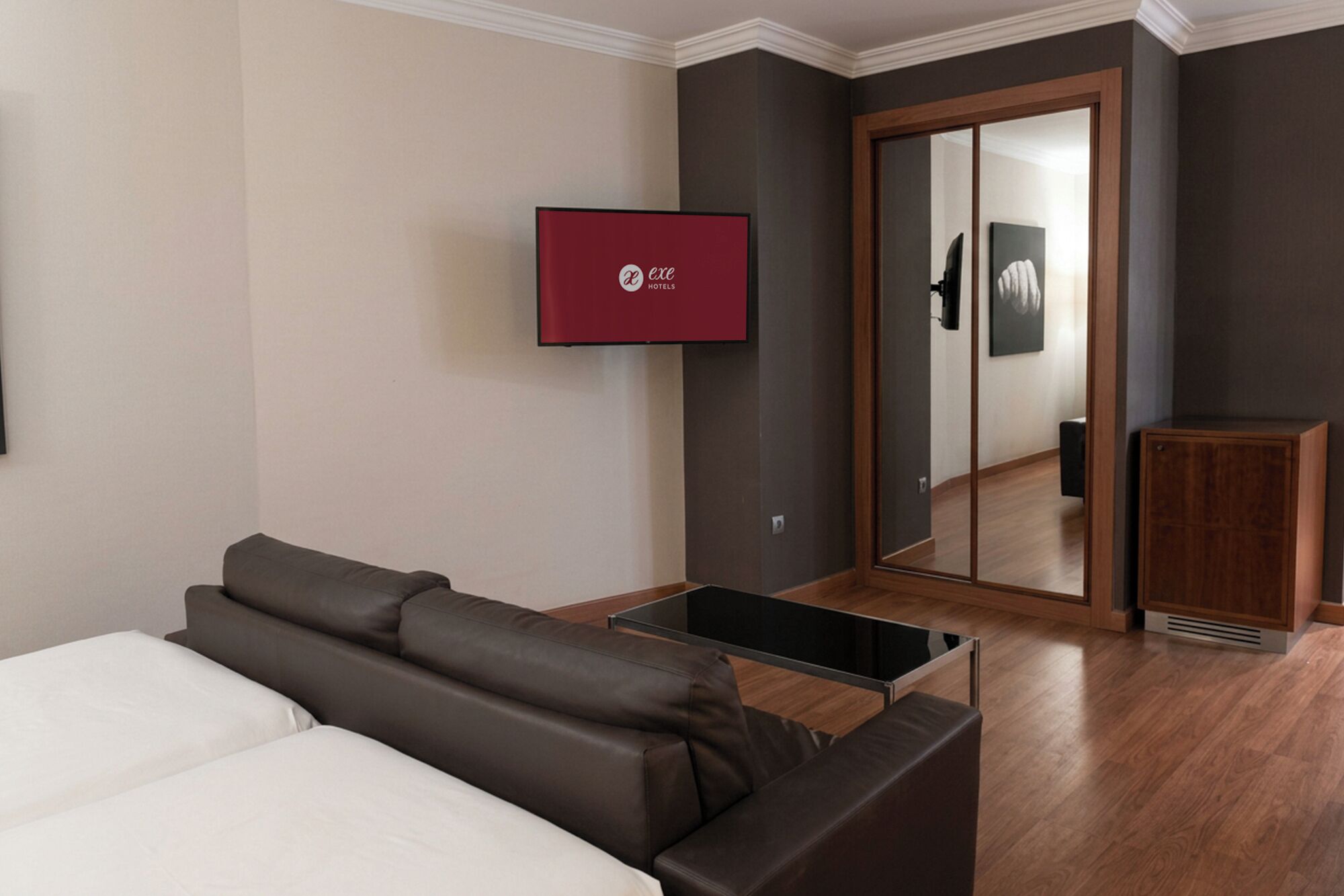 Een hotelkamer met een bank, een aan de muur bevestigde televisie, een spiegel en een houten kast.