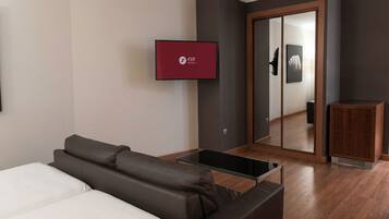 Een hotelkamer met een bank, een aan de muur bevestigde televisie, een spiegel en een houten kast.