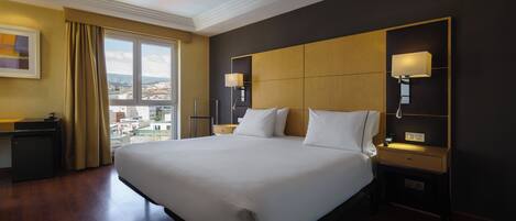 A hotel room with a large bed, two bedside tables, a desk, and a view of the city.