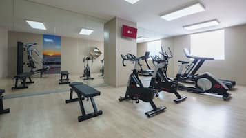 Un gimnasio con equipo de ejercicio, un espejo grande y un televisor en la pared.