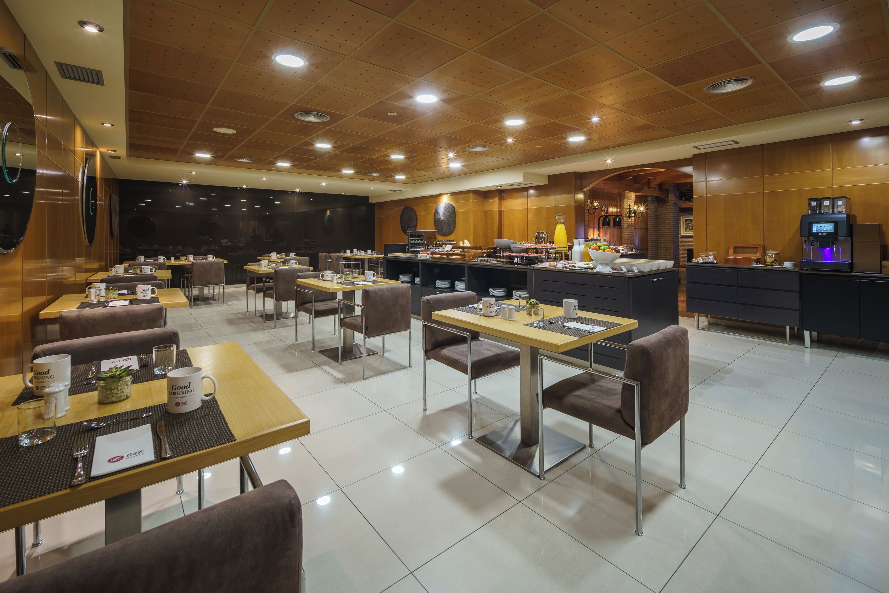 Un restaurante moderno con paneles de techo de madera, varias mesas de comedor con sillas y una zona de bar con electrodomésticos de cocina.