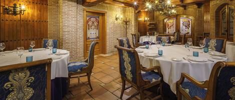 A dining area with wooden tables and chairs, a chandelier, and a brick wall.