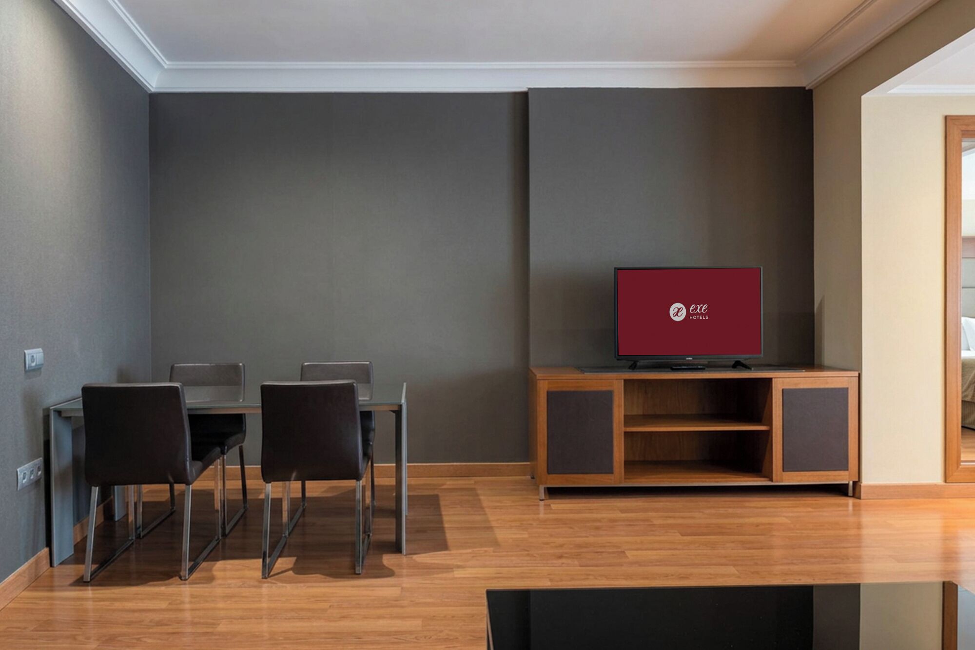 A modern hotel room with a dining area, a flat-screen TV, and a wooden cabinet.