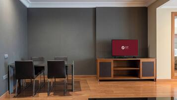 A modern hotel room with a dining area, a flat-screen TV, and a wooden cabinet.