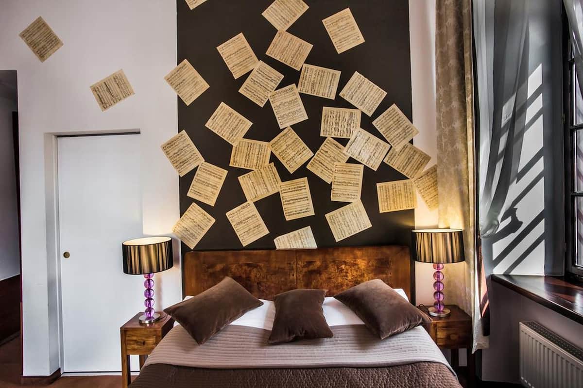 A hotel room with a bed, two bedside tables, a wall with notes, a door, and a window with curtains.