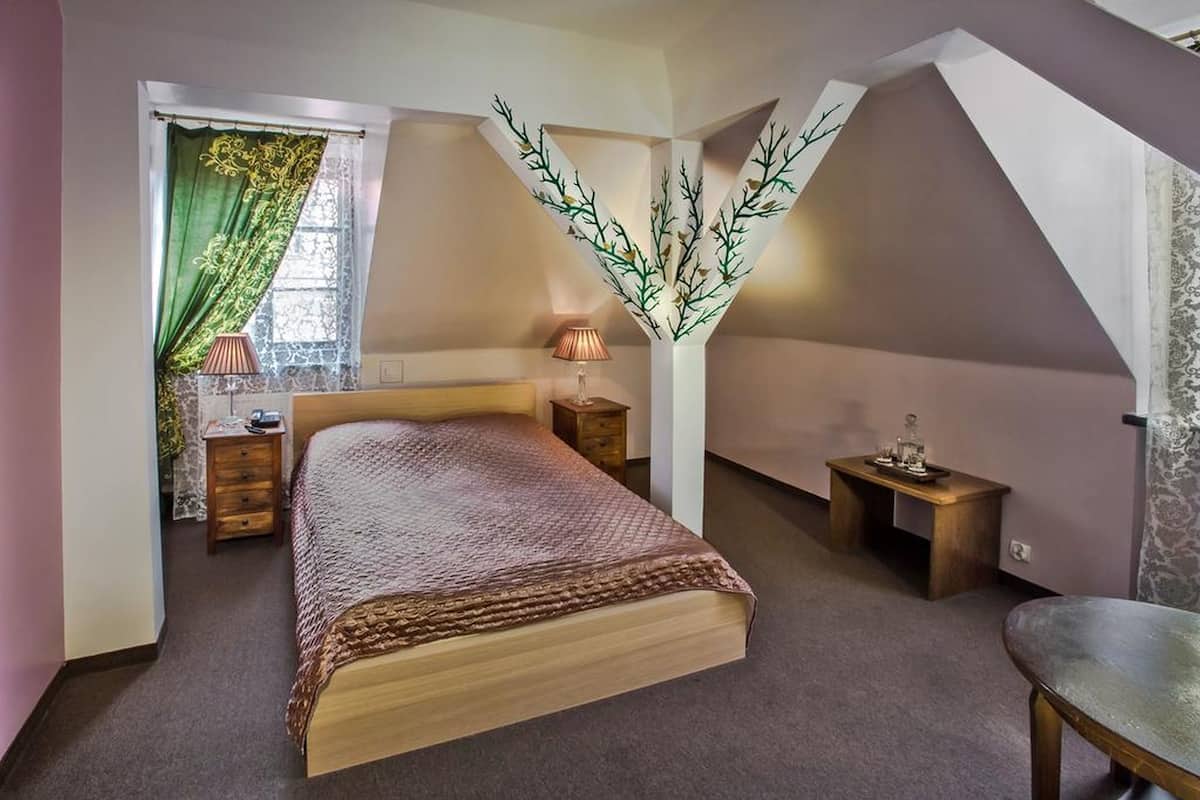 A bedroom with a bed, a nightstand, a dresser, a window with curtains, and a wall-mounted light fixture.