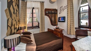 A hotel room with a bed, a desk, a chair, a lamp, a TV, and a window with curtains. - Castle Inn (Warsaw)