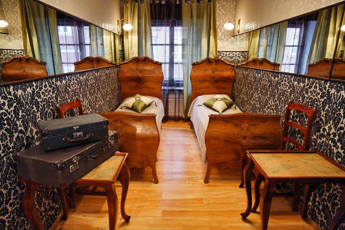 A room with two beds, a table, and a chair. There is a suitcase on the table.