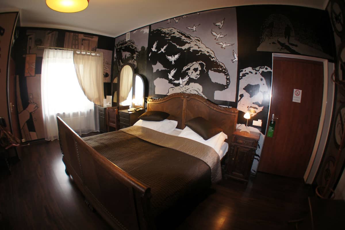 A bedroom with a large bed, a nightstand, a mirror, and a wall mural.